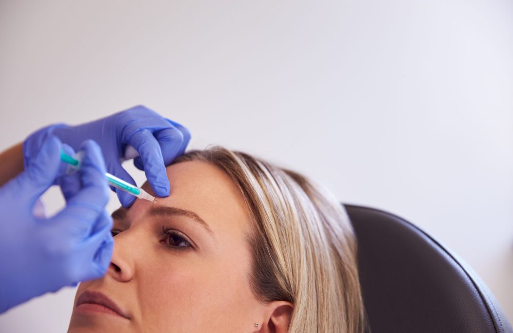 Woman Sitting In Chair Being Give Botox Injection In Forehead By Female Doctor